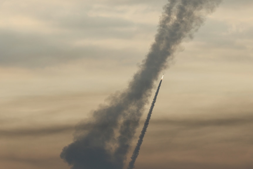 A rocket travels upward in the sky with smoke behind it