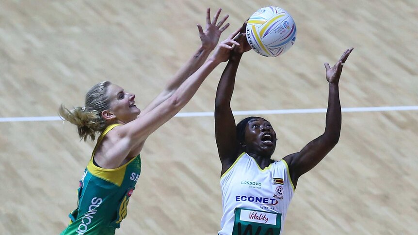 A female netball player lunges to her left as she tries to catch the ball standing next to her opponent.