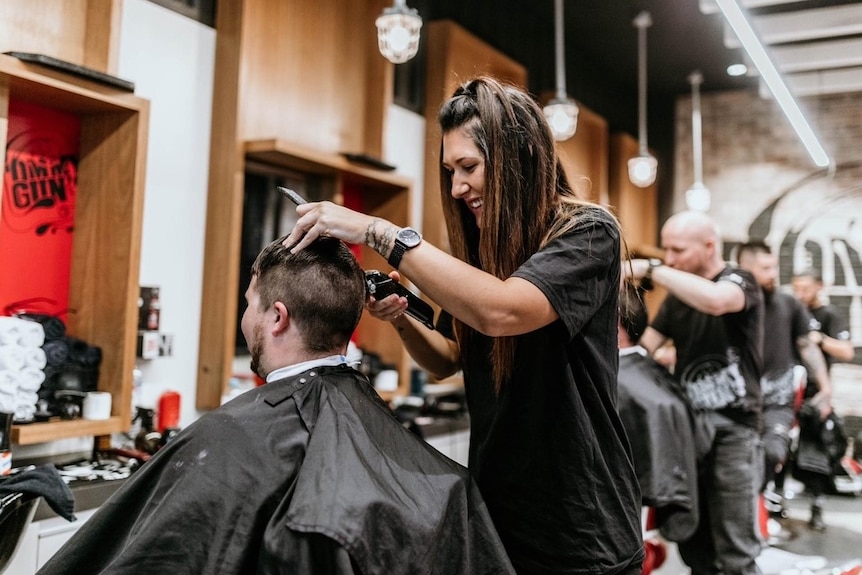A woman cuts a man's hair in a salon. 