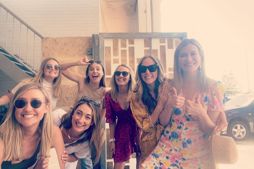 A group of seven blonde women in sunglasses pose for a group photo.