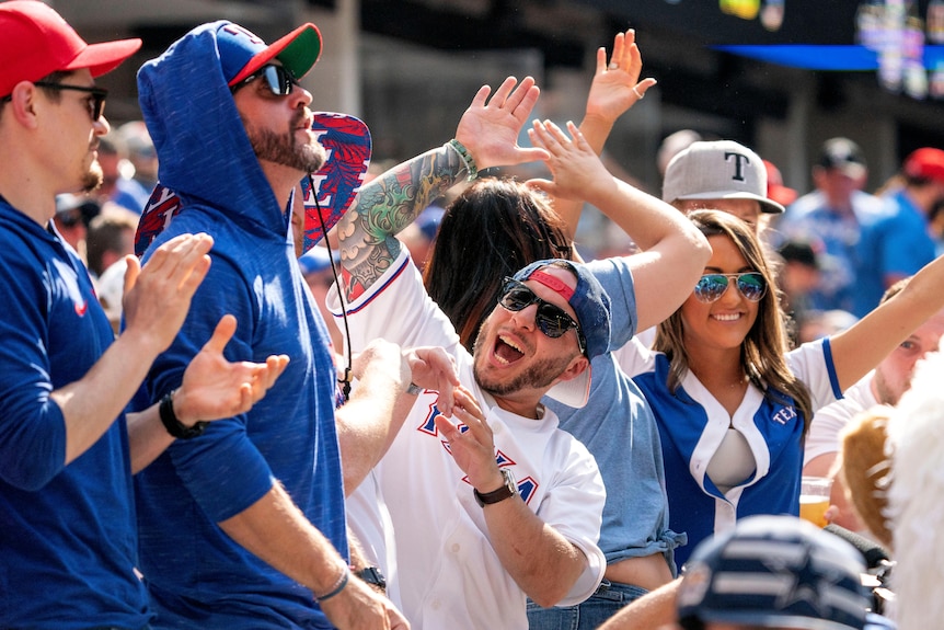 Men and women wearing blue and white smile and raise their hands without wearing masks