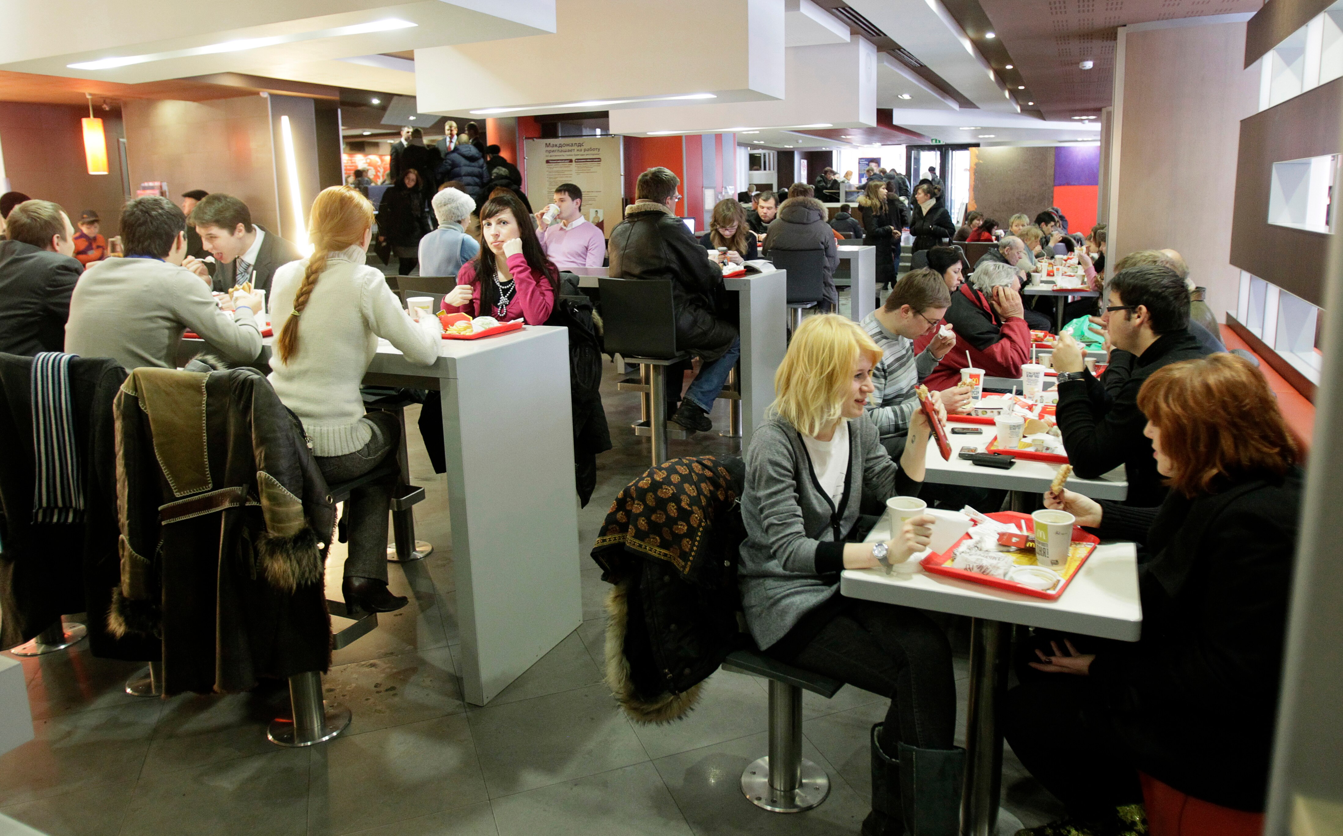 People sit indoors at tables eating food that sits on red plastic trays