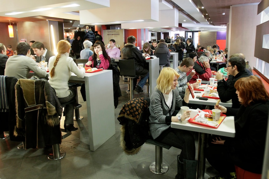 People sit indoors at tables eating food that sits on red plastic trays