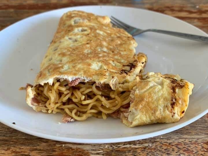 An omelette on a plate, filled with noodles and bacon.