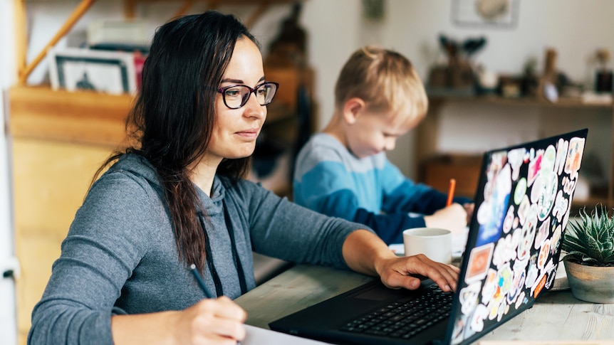 Woman working at home with a kid and a laptop in a story about stepping back and the benefits.