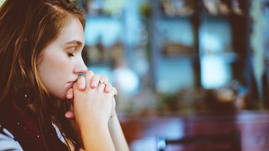 Young woman with eyes closed and hands clasped, praying.