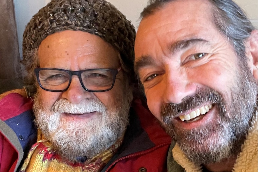Close up photo of smiling man on left with beard, beanie and glasses and younger man on right with beard also smiling.