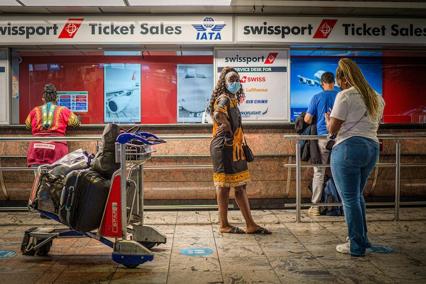 A woman in a face mask stands near a check-in counter at an airport 