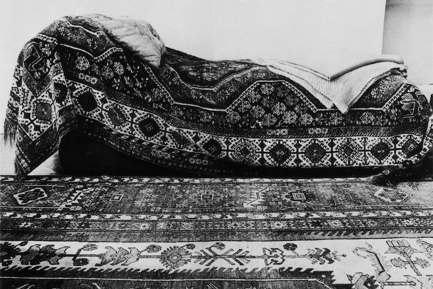 A black-and-white image of a couch covered in a patterned blanket.