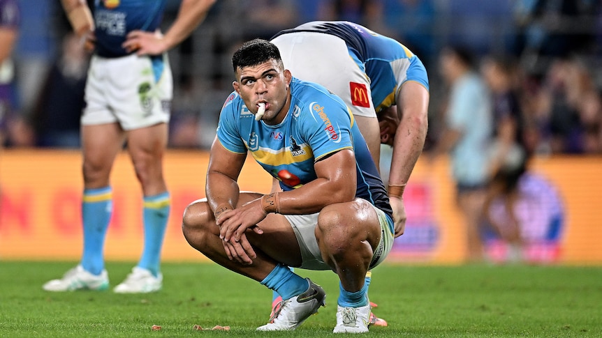 NRL player David Fifita, on his haunches, with his mouth guard hanging from his mouth, has he look tired and disappointed