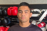 A man in front of a rack of boxing gloves