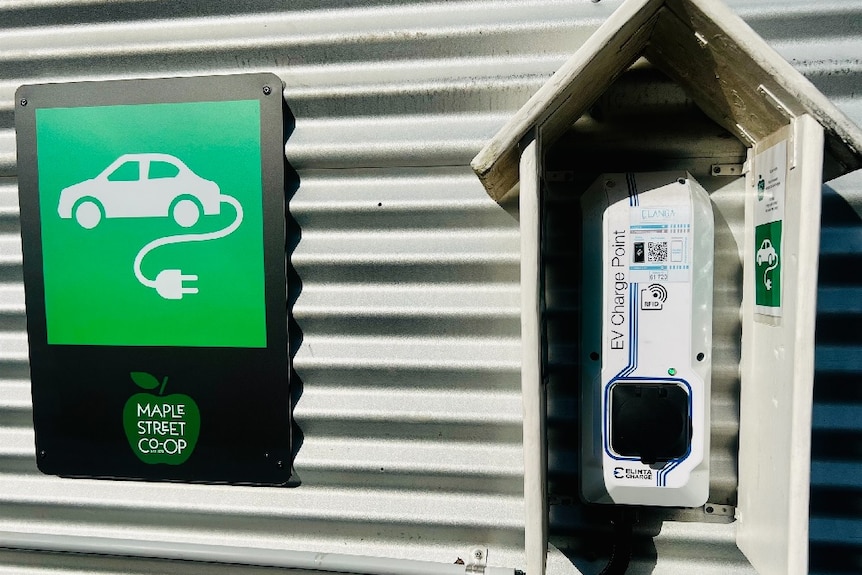 A wall-mounted car charging point with a green and white car sign