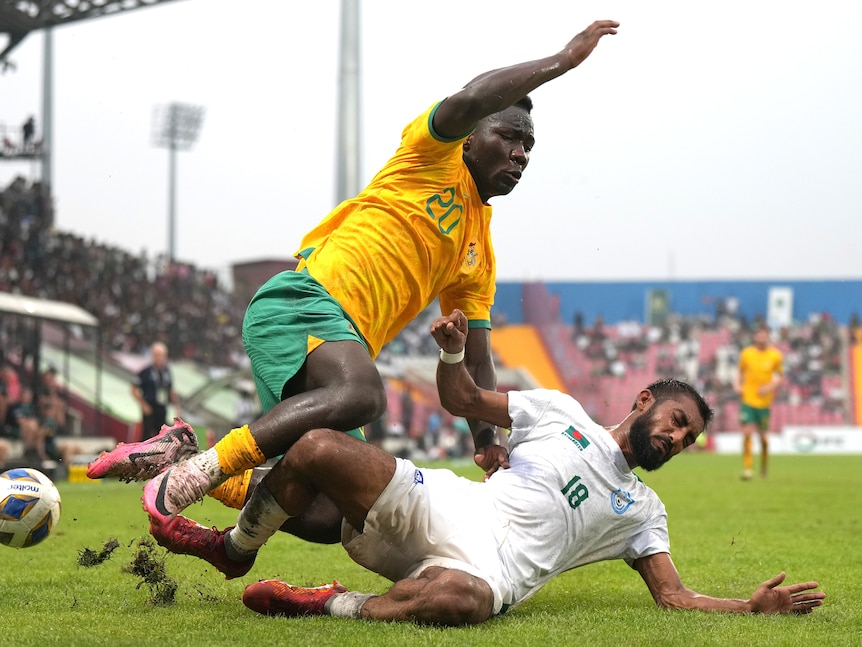 A soccer player slides under another player to get to the ball during a match