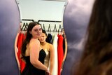 A girl trying on a formal dress checking herself out in a curved mirror