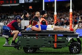 An AFL player lies on a stretcher and is carted off with support staff around him.