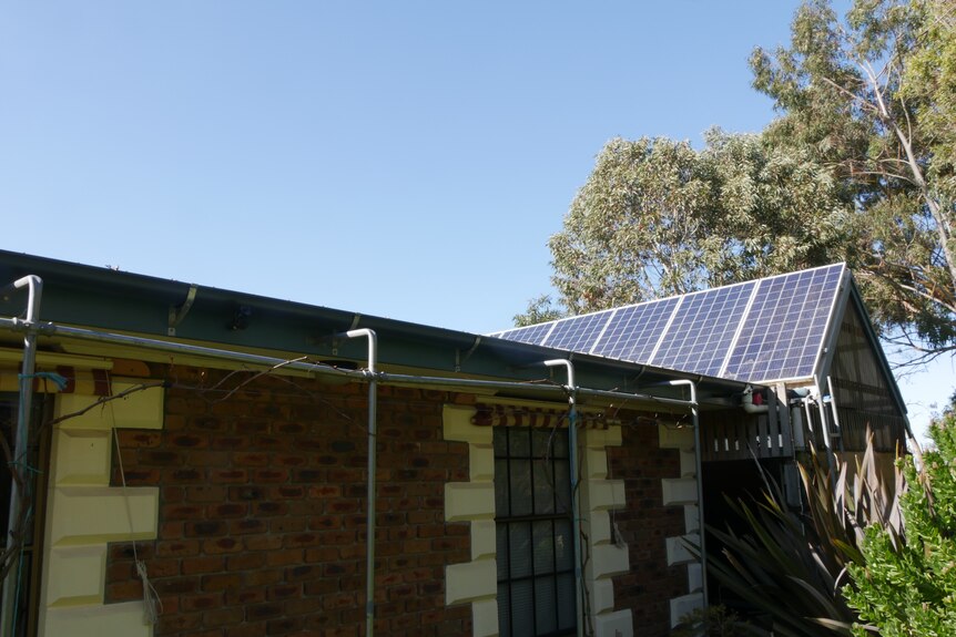 Multiple solar panels sit on the roof of a brick home