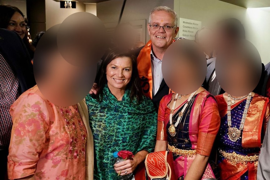 Scott Morrison, wearing an orange scarf, pose with wife Jenny and female dancers in traditional Indian costume.
