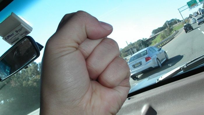 A man's fist being waved at another road user in the front of a car.