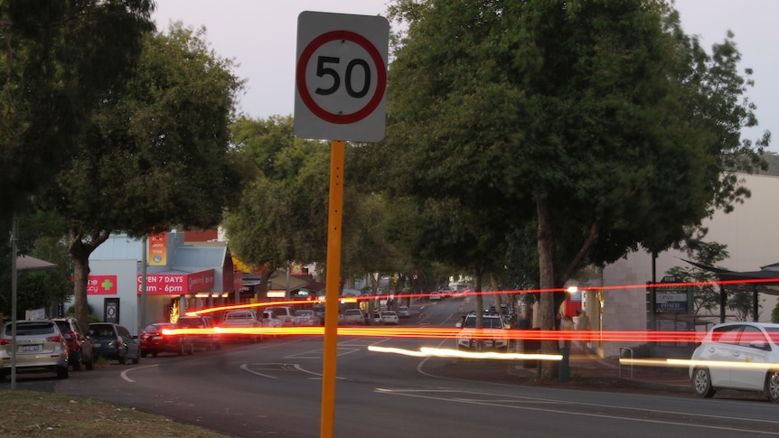 A dimly lit view of margaret rivers main road through town with a 50 kilometre speed sign and flashing lights from cars going by
