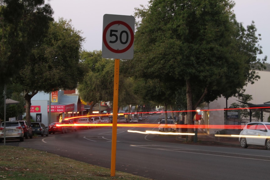 A dimly lit view of margaret rivers main road through town with a 50 kilometre speed sign and flashing lights from cars going by