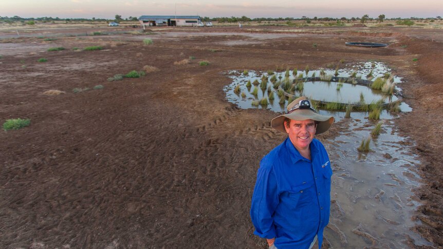 Ecologist Rob Wager stands in front of a sparse landscape dotted with a small fresh water spring.