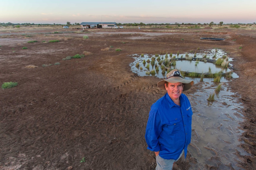 Ecologist Rob Wager stands in front of a sparse landscape dotted with a small fresh water spring.