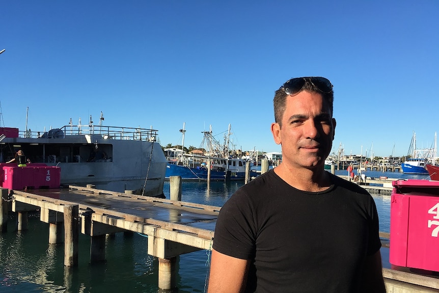 Fisherman Pavo Walker stands on a wharf with fishing vessels in the background.