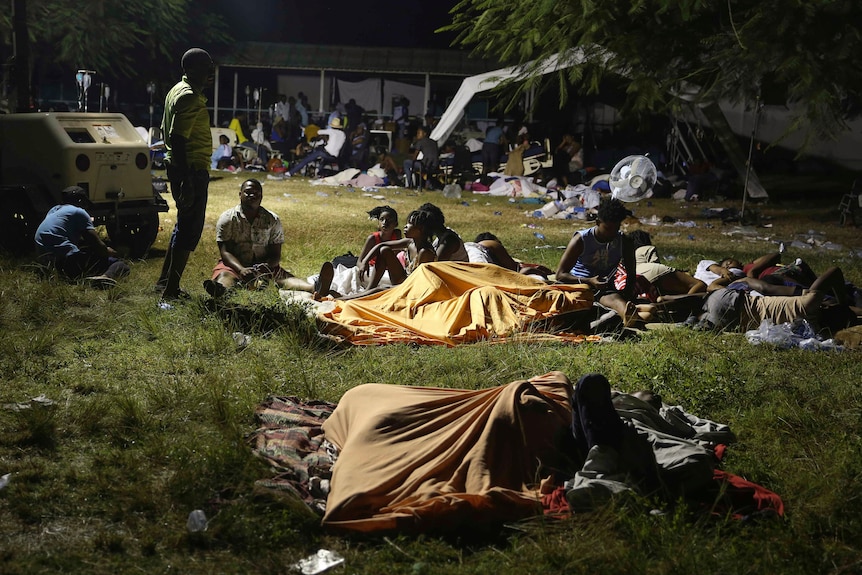 People spend the night outdoors in a grassy area, some with light blankets and shelter and others out in the open.