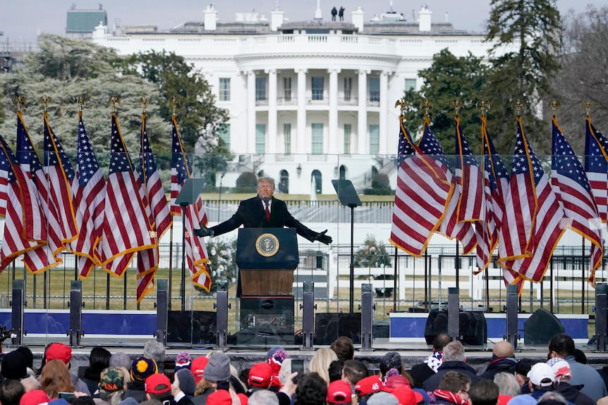 Donald Trump con le braccia tese mentre si trova su un podio all'aperto di fronte alla Casa Bianca 