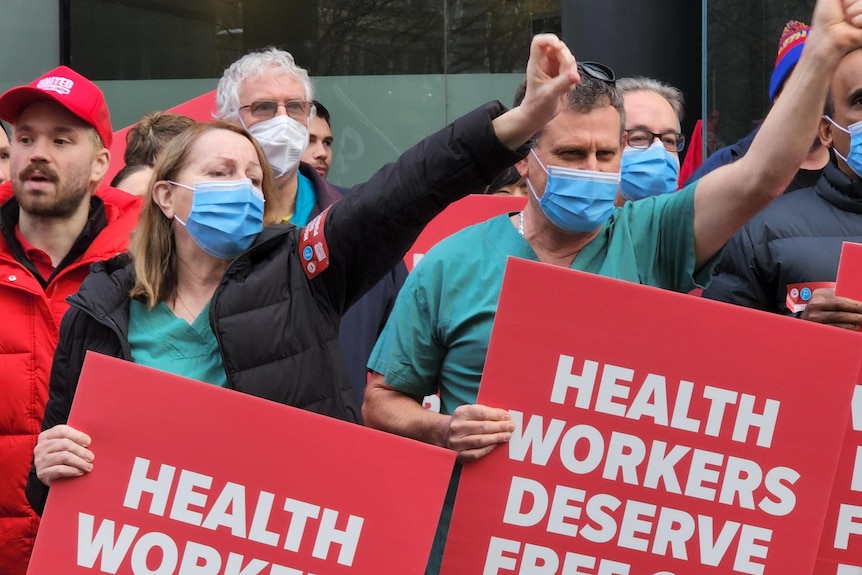 Protestors in hospital scrubs holding red placards