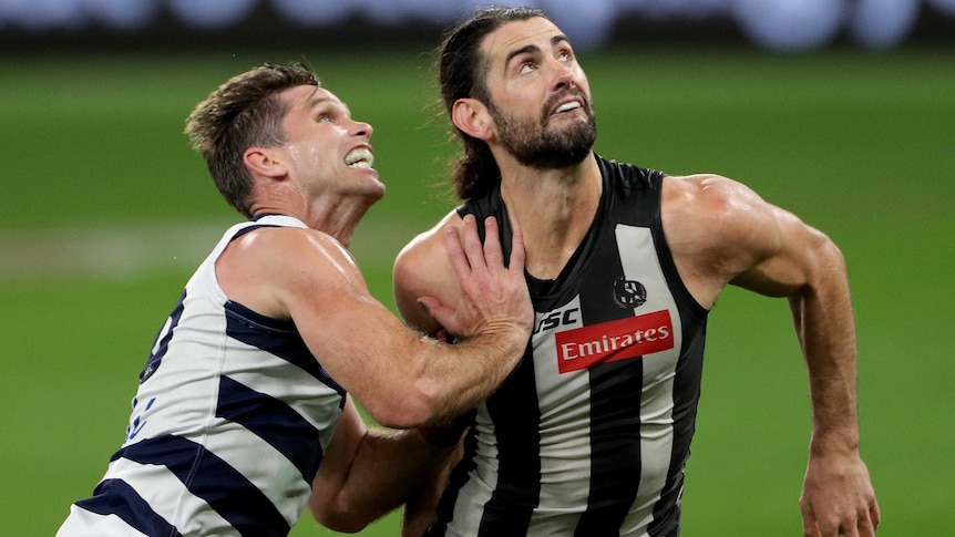 A Geelong AFL player pushes against a Collingwood opponent as they prepare to contest for the ball in Perth.