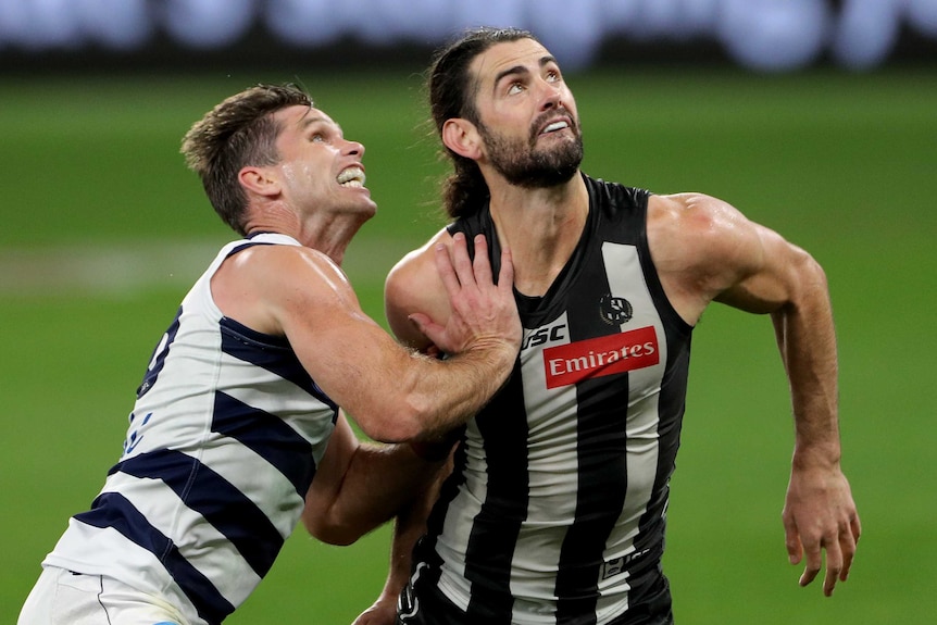 A Geelong AFL player pushes against a Collingwood opponent as they prepare to contest for the ball in Perth.