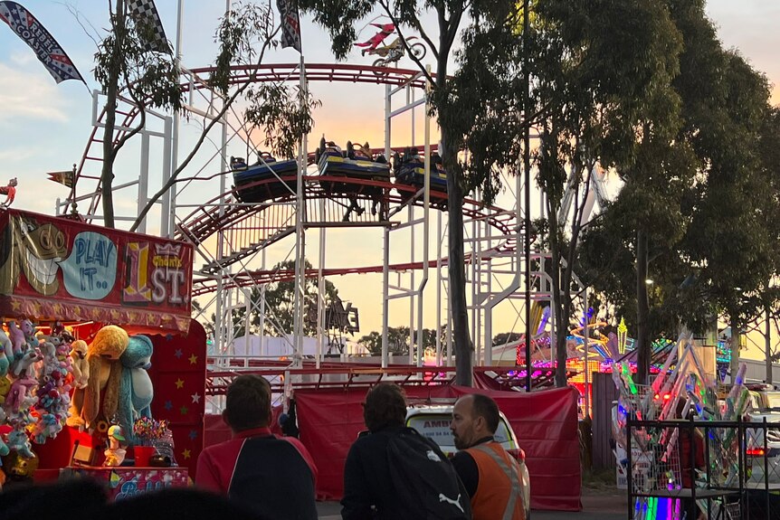 A novelty stand in front of a rollercoaster at a show with evening sunset behind