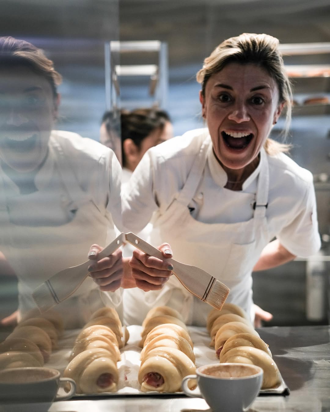 Woman in chef white shirt smiles big coating pastry in egg wash
