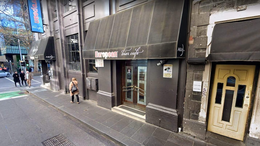 The black exterior of the European Bier Cafe in Melbourne, with some unidentifiable people walking past.