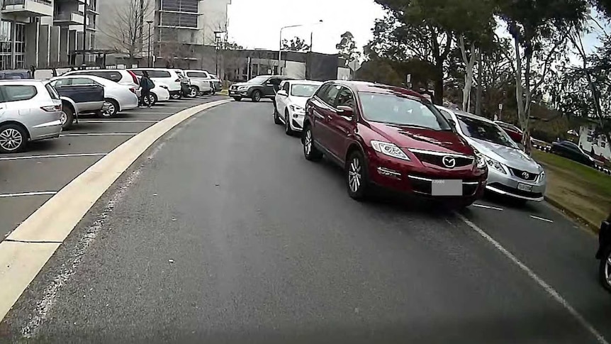 A maroon car double-parked, blocking a street.