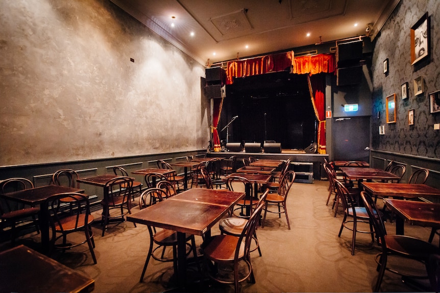 An empty room with tables and chairs in the front and a stage at the back