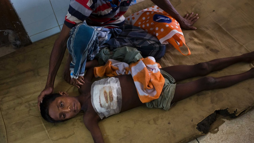 A child lies on the floor next to his father at a Cox's Bazar hospital. The boy got a bullet injury in the chest fleeing Myanmar