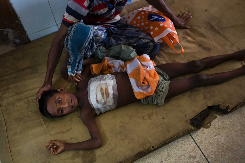 A child lies on the floor next to his father at a Cox's Bazar hospital. The boy got a bullet injury in the chest fleeing Myanmar