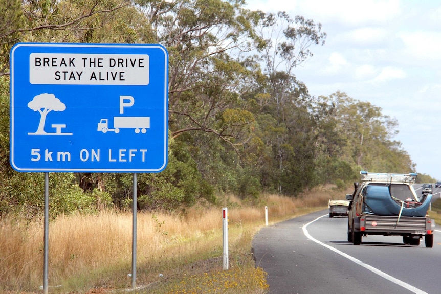 Cars drive past a rest stop sign beside a highway.