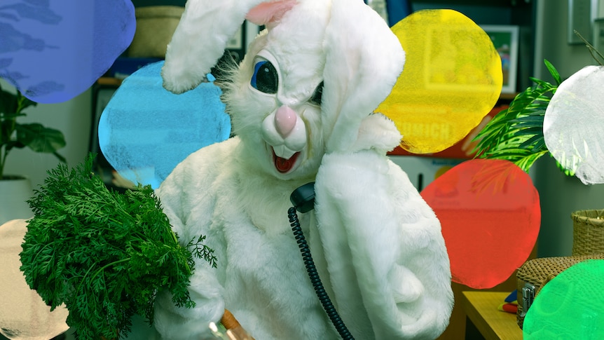 Someone in an Easter bunny costume talks on the phone while holding a bunch of carrots.
