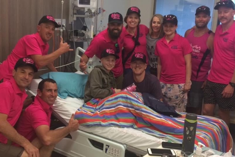 Jacob Cooper in a hospital bed surrounded by people in fluro pink shirts 