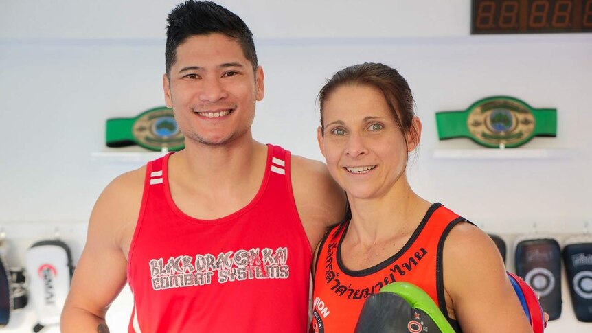 A man and woman stand in a boxing gym side by side smiling at the camera.
