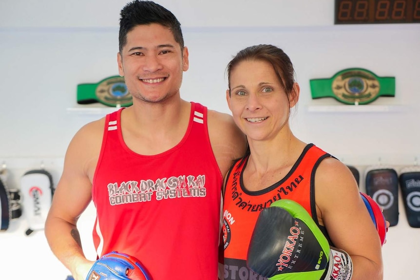 A man and woman stand in a boxing gym side by side smiling at the camera.