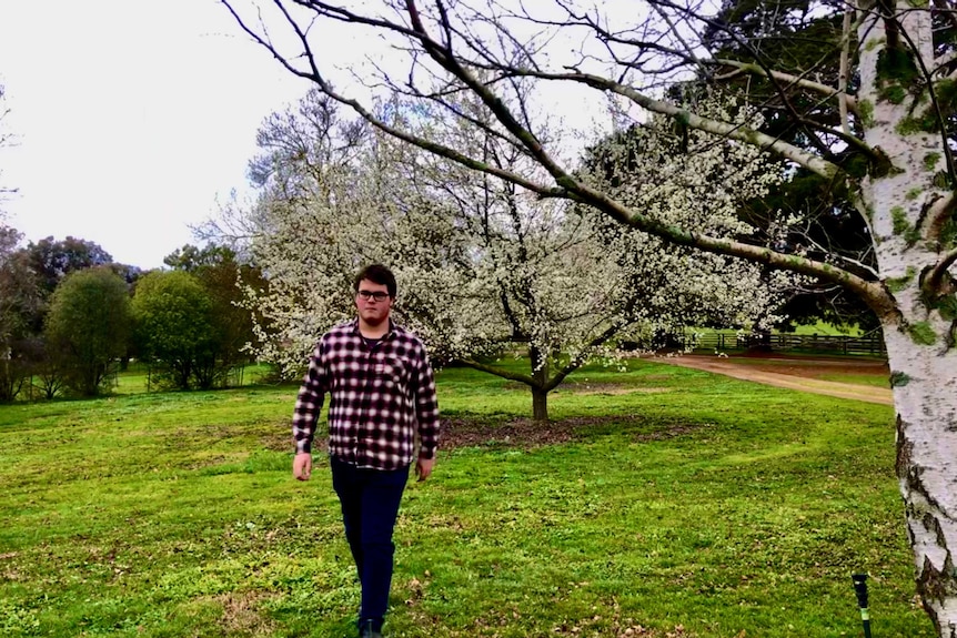 teenager walks through farm surrounded by trees