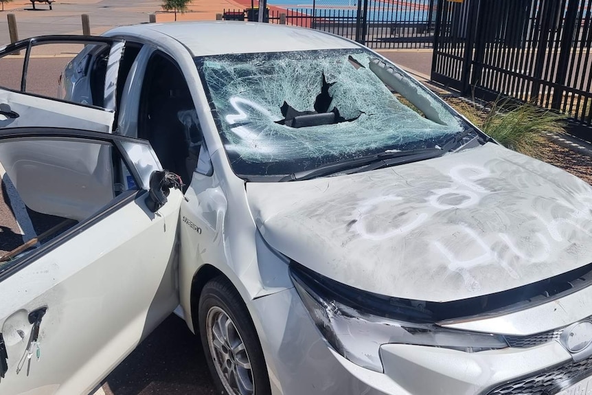 A light-coloured sedan with a smashed windscreen, severe panel damage and spray-paint on its bonnet.