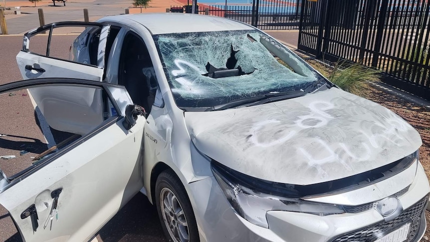 A vandalised white car with smashed windows.