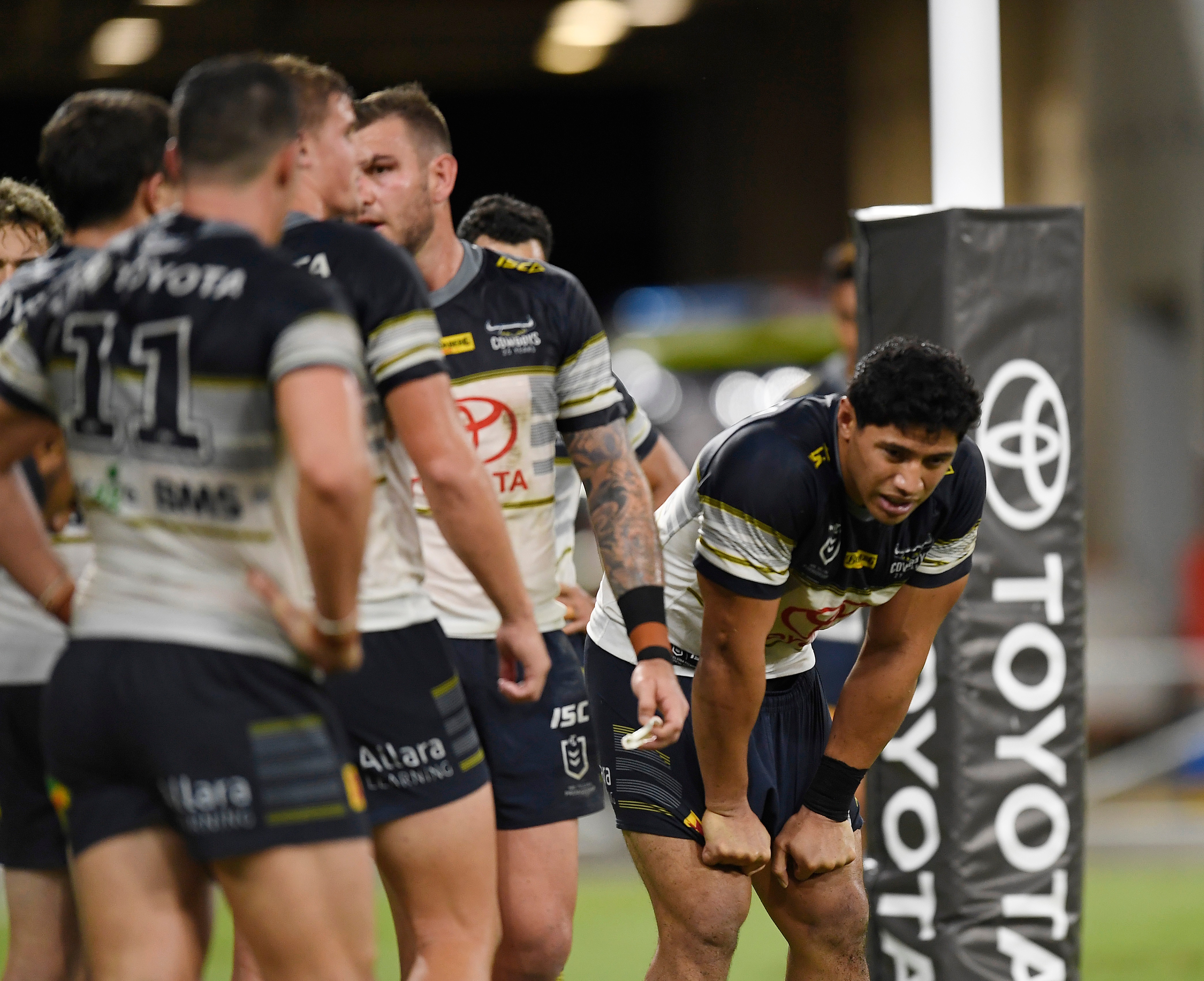 Jason is slumped over during a rugby league match, other teammates stand around in black and white. Toyota sign.