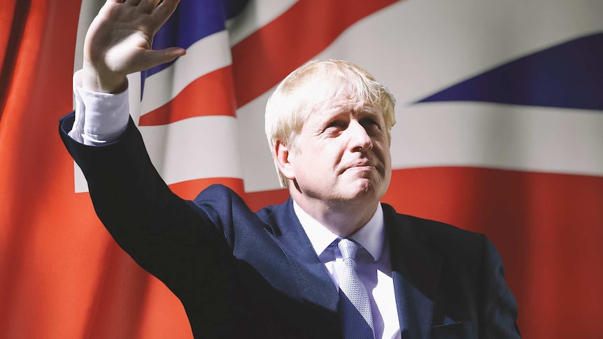Boris Johnston gestures a waves in front of a UK flag.