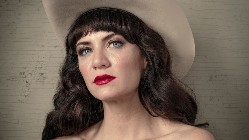 A headshot of nikki lane, who wears red lipstick and a wide brimmed hat
